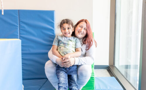 Therapist hugs child in recreational therapy gym.