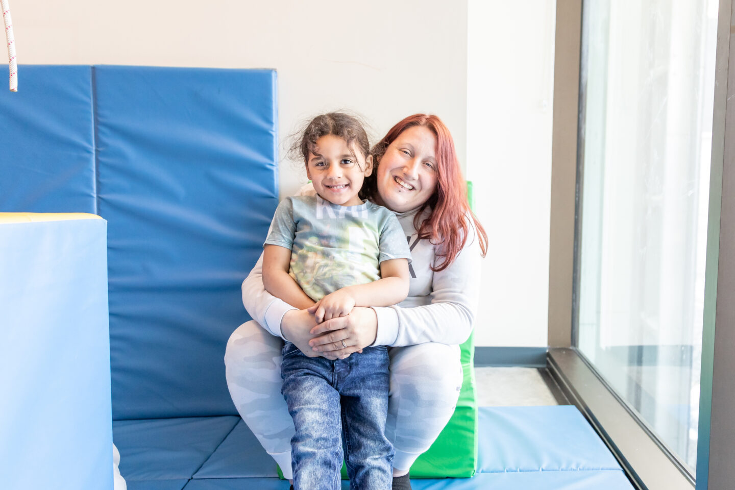 Therapist hugs child in recreational therapy gym.