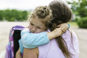 child hugging adult woman; woman is shown from behind. Child is wearing a backpack.