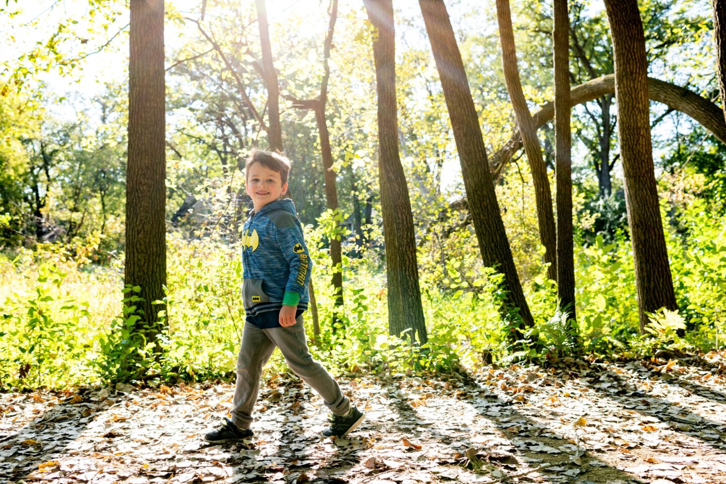 little boy walks smiling through the woods